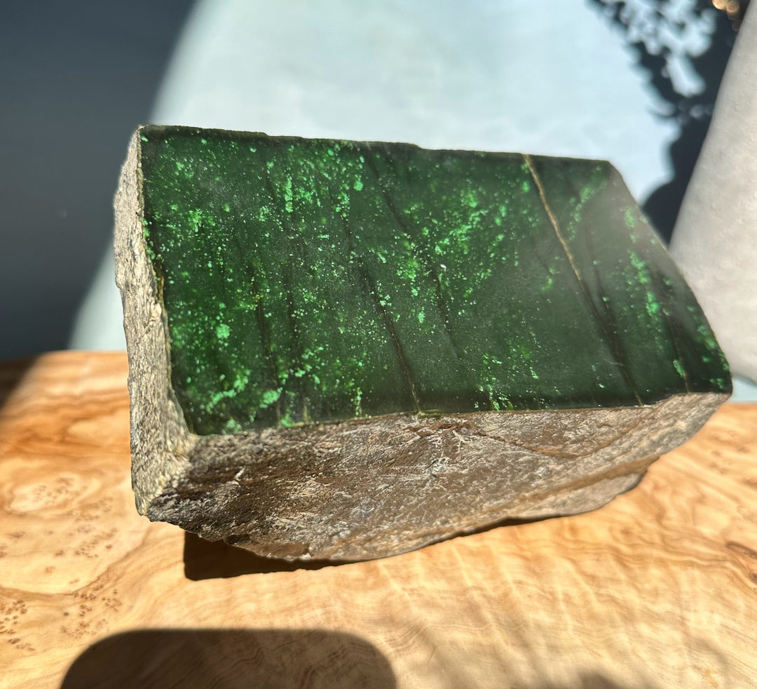Cassiar Jade rough block shown from the side with dark green interior and bright speckles; green ruler for scale.