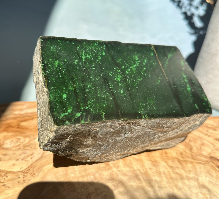 Cassiar Jade rough block shown from the side with dark green interior and bright speckles; green ruler for scale.