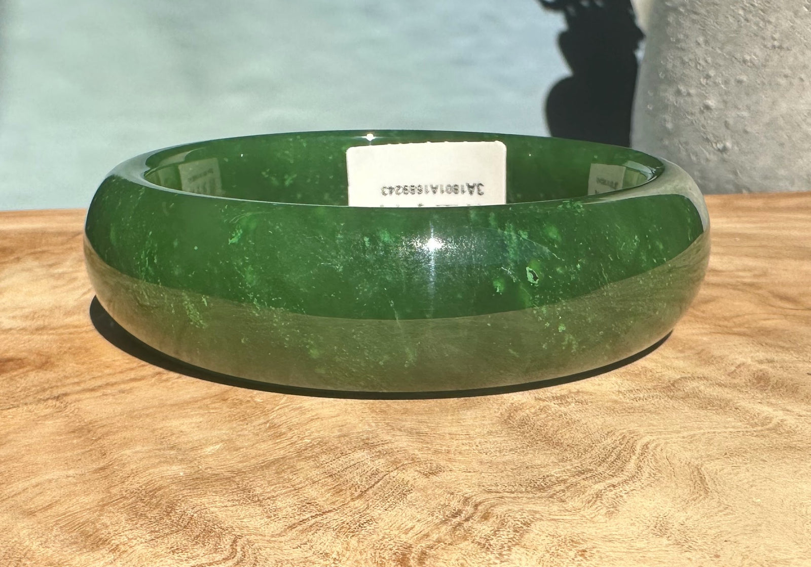 A+ Canadian jade bangle in bright green with inner label visible on a wooden surface