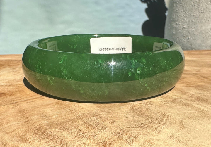 A+ Canadian jade bangle in bright green with inner label visible on a wooden surface
