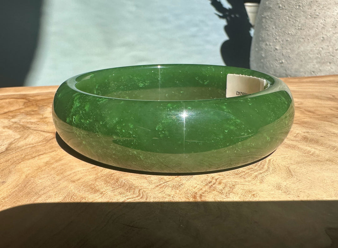 A+ Canadian jade bangle in vivid green resting on a wooden surface.