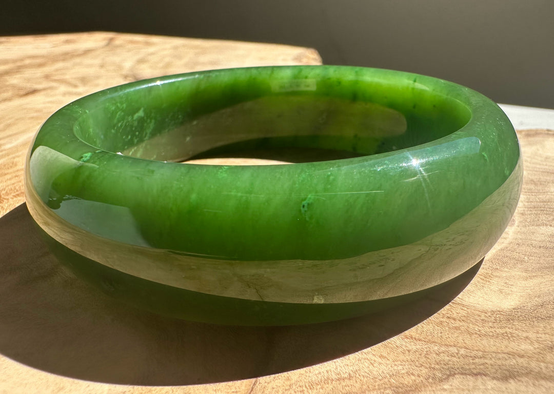 Green jade bangle with a lighter inner edge resting on a wooden surface.