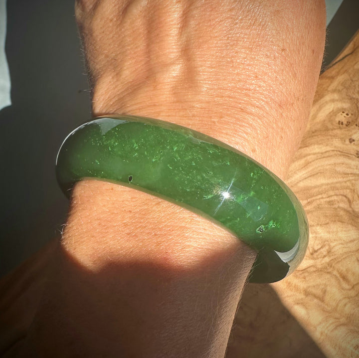 Green jade bangle worn on the wrist with a polished surface in bright light.