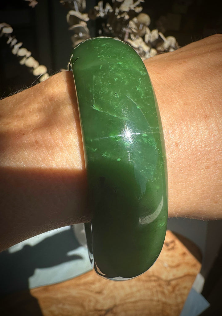 Close up of green jade bangle on the wrist showing vivid color and glossy finish.