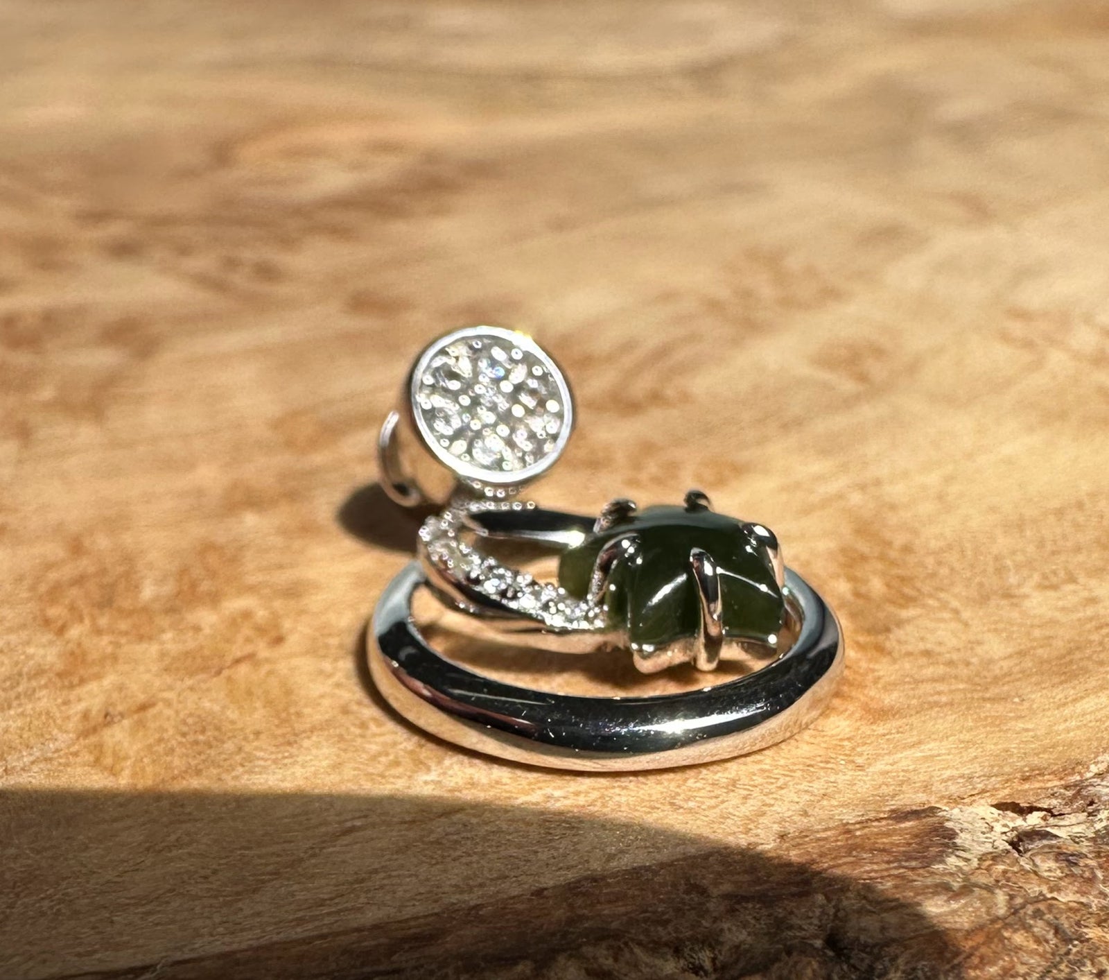 Close up of the pendant on wood highlighting the crystal round cap and dark green jade star within the crescent and circular setting