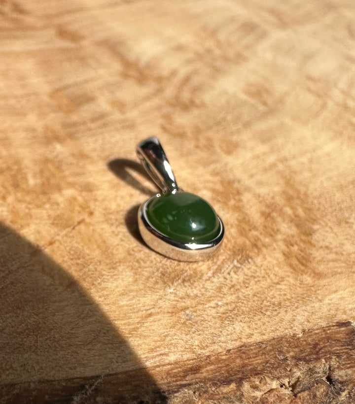 Dainty Silver and Jade Pendant 6mm with round green jade in a silver bezel and bail on a wood surface.