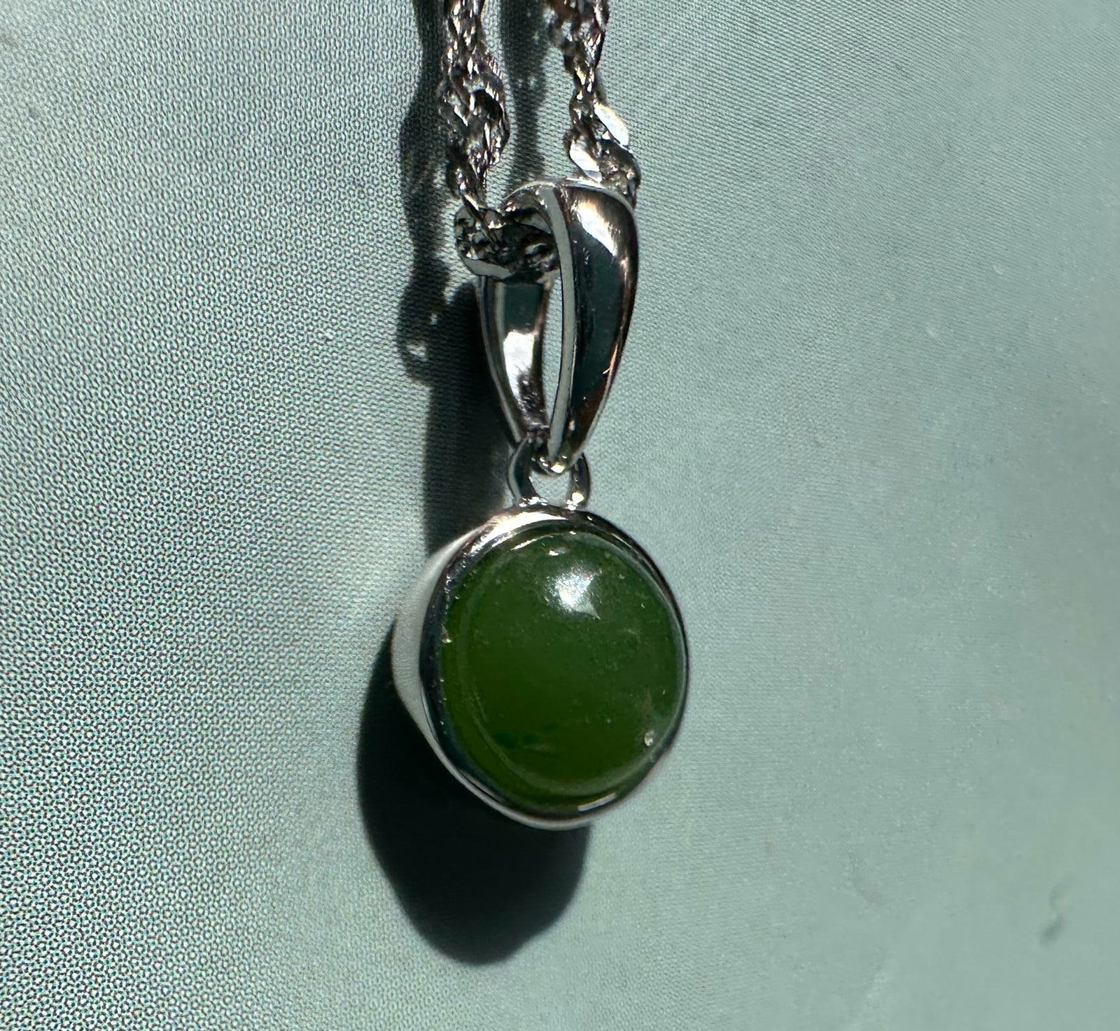 Dainty Silver and Jade Pendant with round green jade cabochon set in a polished silver bezel hanging from a chain.