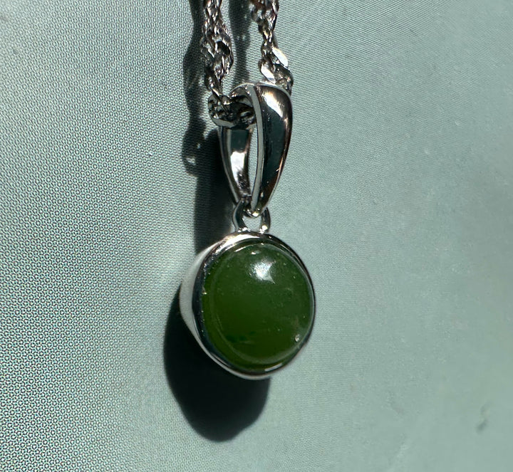 Dainty Silver and Jade Pendant with round green jade cabochon set in a polished silver bezel hanging from a chain.