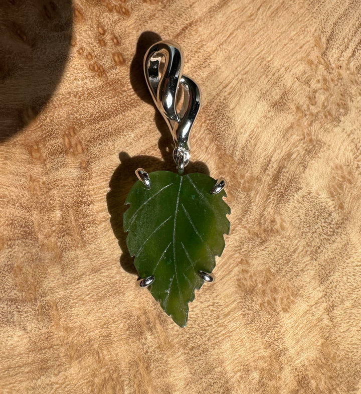 Green leaf pendant in a silver setting with four prongs and a twisted bail on a wood surface