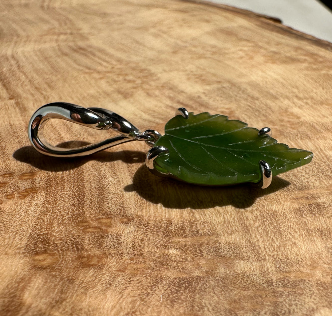 Green leaf pendant with silver prongs on a warm wooden surface with the chain nearby