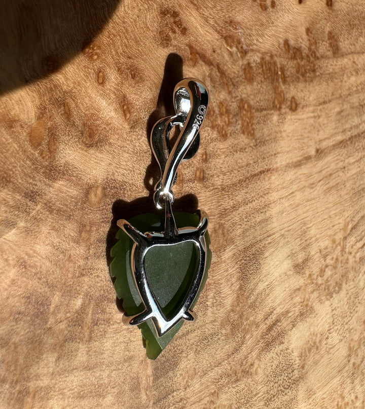 Silver leaf pendant with green center resting on textured wood background