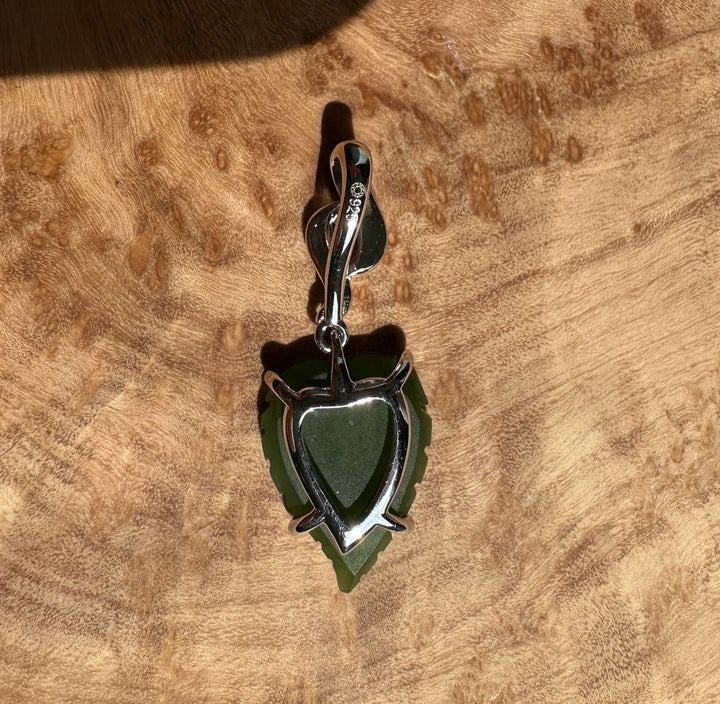 Silver leaf pendant with green center beside a US quarter for scale on wood surface