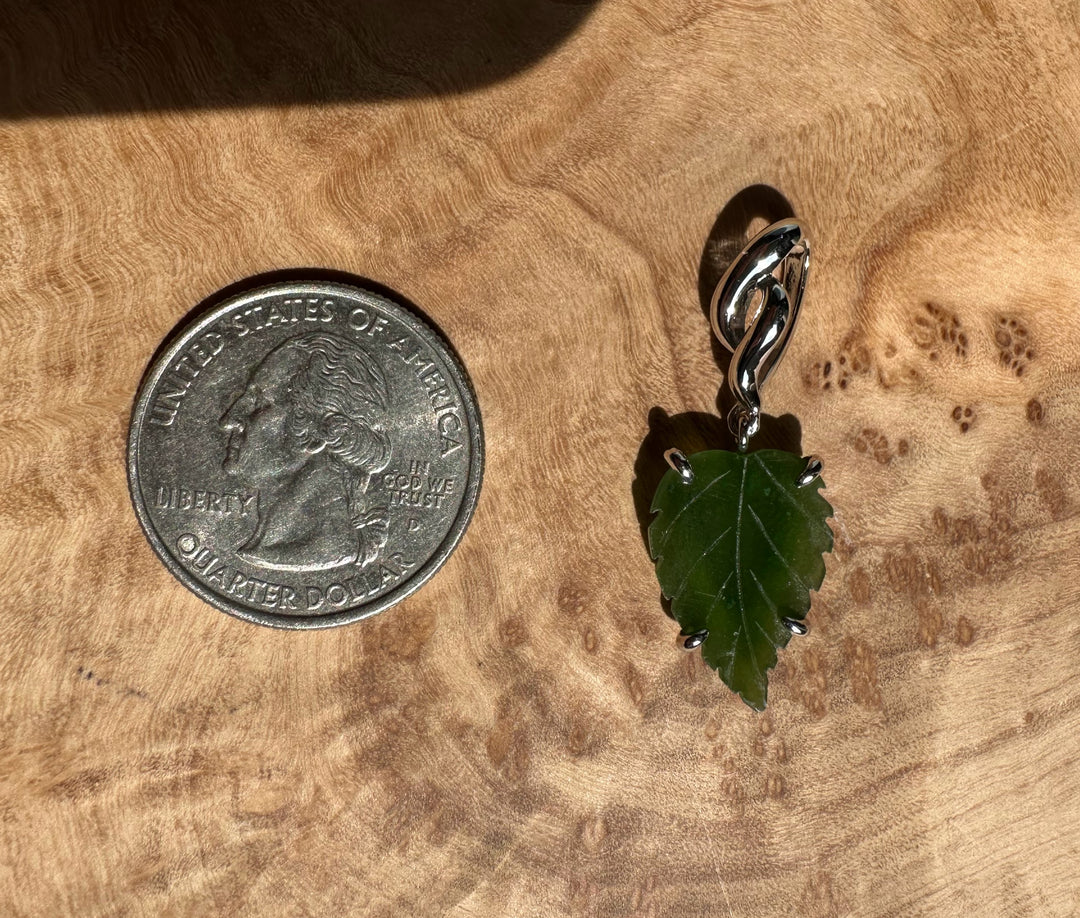 Close up of silver leaf pendant with green center hanging from a curved bail on wood background