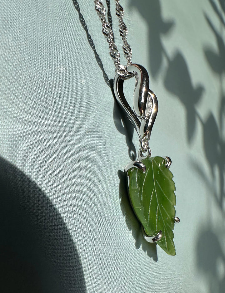 Green leaf pendant with curved silver bail and chain against a pale blue backdrop