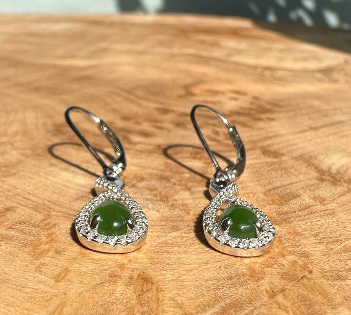 Close-up of Canadian Jade and Silver Infinity Twist Earrings showing emerald green jade drops within sparkling halos on wood surface