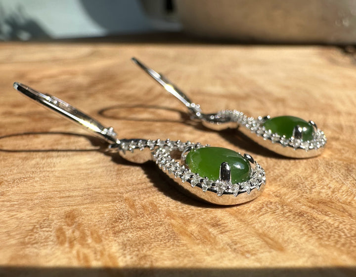 Canadian Jade and Silver Infinity Twist Earrings with green jade teardrops framed by a crystal pavé halo on a wooden surface.