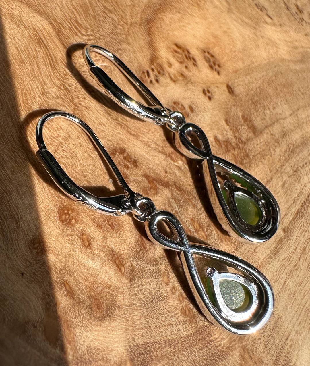 Pair of Canadian Jade and Silver Infinity Twist Earrings on a display bar, each with a green jade teardrop surrounded by pavé crystals.