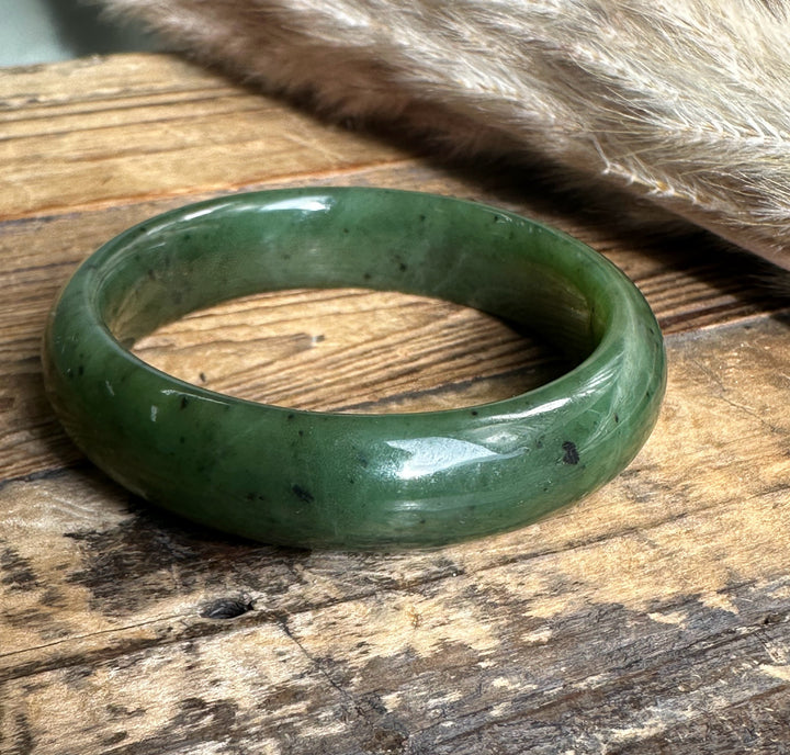 Green jade bangle with dark flecks seen at a slight angle on weathered wood