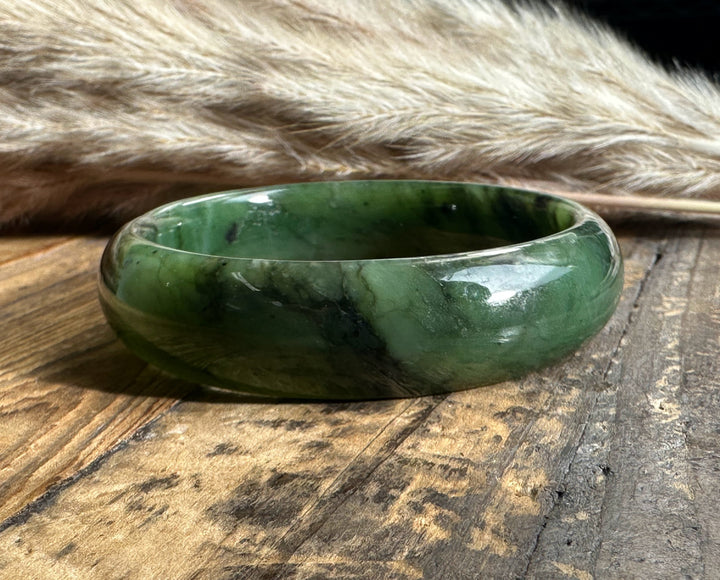 Closeup of a wide green jade bangle with rich color and dark inclusions on a wooden surface