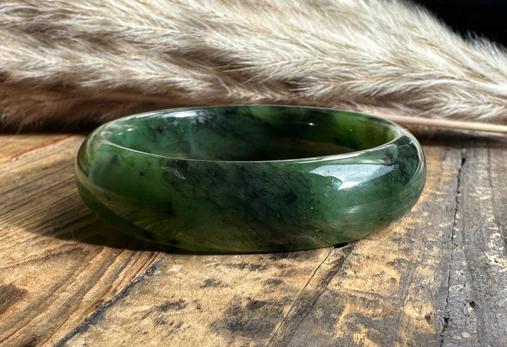 Wide jade bangle in green with marbled patterns on a weathered wood background