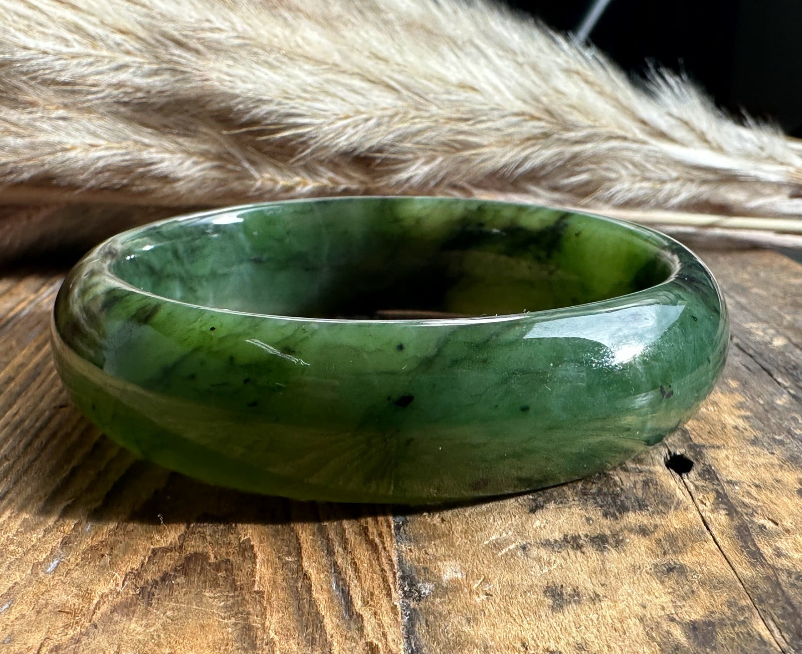 Wide green jade bangle with dark veining resting on a rustic wooden surface