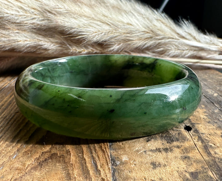 Wide green jade bangle with dark veining resting on a rustic wooden surface