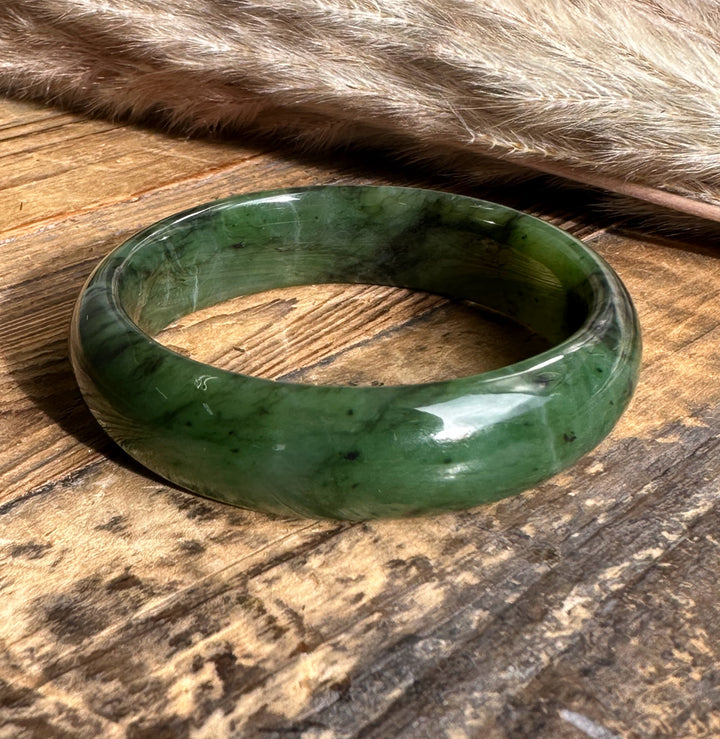 15mm wide jade bangle in deep green resting on a rustic wooden surface with a soft fur backdrop