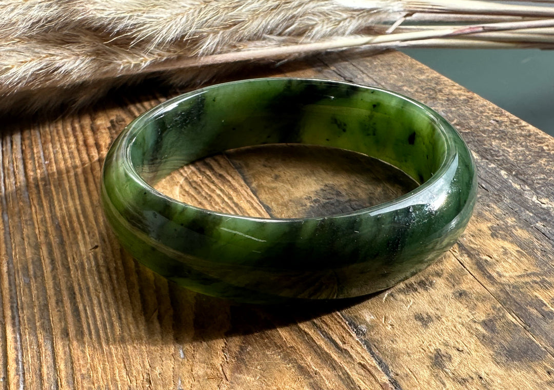 15mm wide jade bangle in green tones viewed from above on a rustic wooden surface