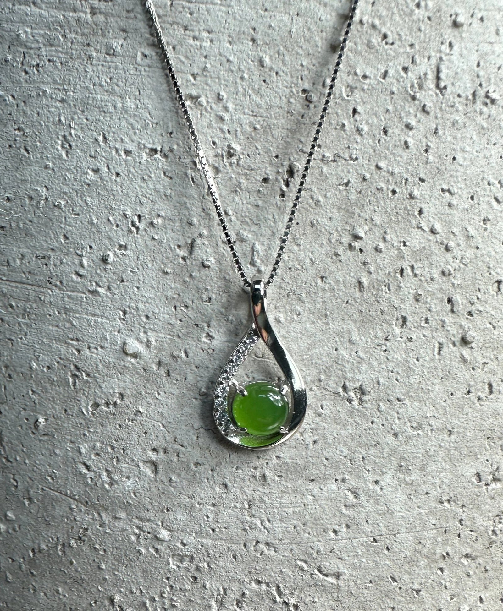 Silver Infinity pendant with a green round gemstone and crystal accents on a necklace