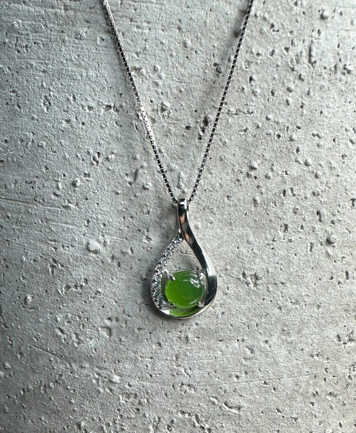 Silver Infinity pendant with a green round gemstone and crystal accents on a necklace