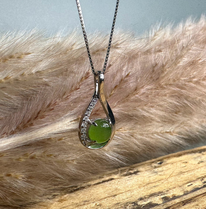 Silver Infinity pendant with a curved edge and a row of small diamonds along one side surrounding a green center stone