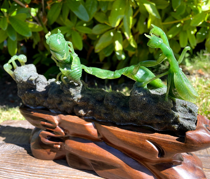 Green praying mantis figurine on a wooden base with a natural background