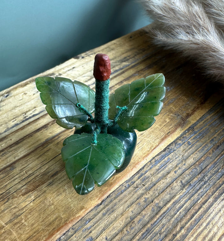 Jade apple carving with glossy green leaves and red stem resting on a wooden surface