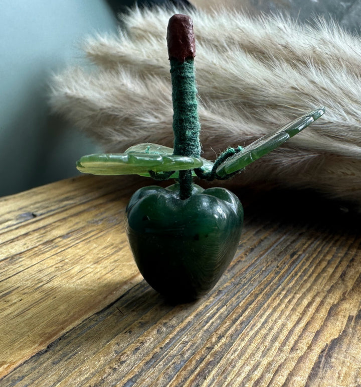 Two inch jade apple carving with a tall green stem and red tip on a wooden surface.