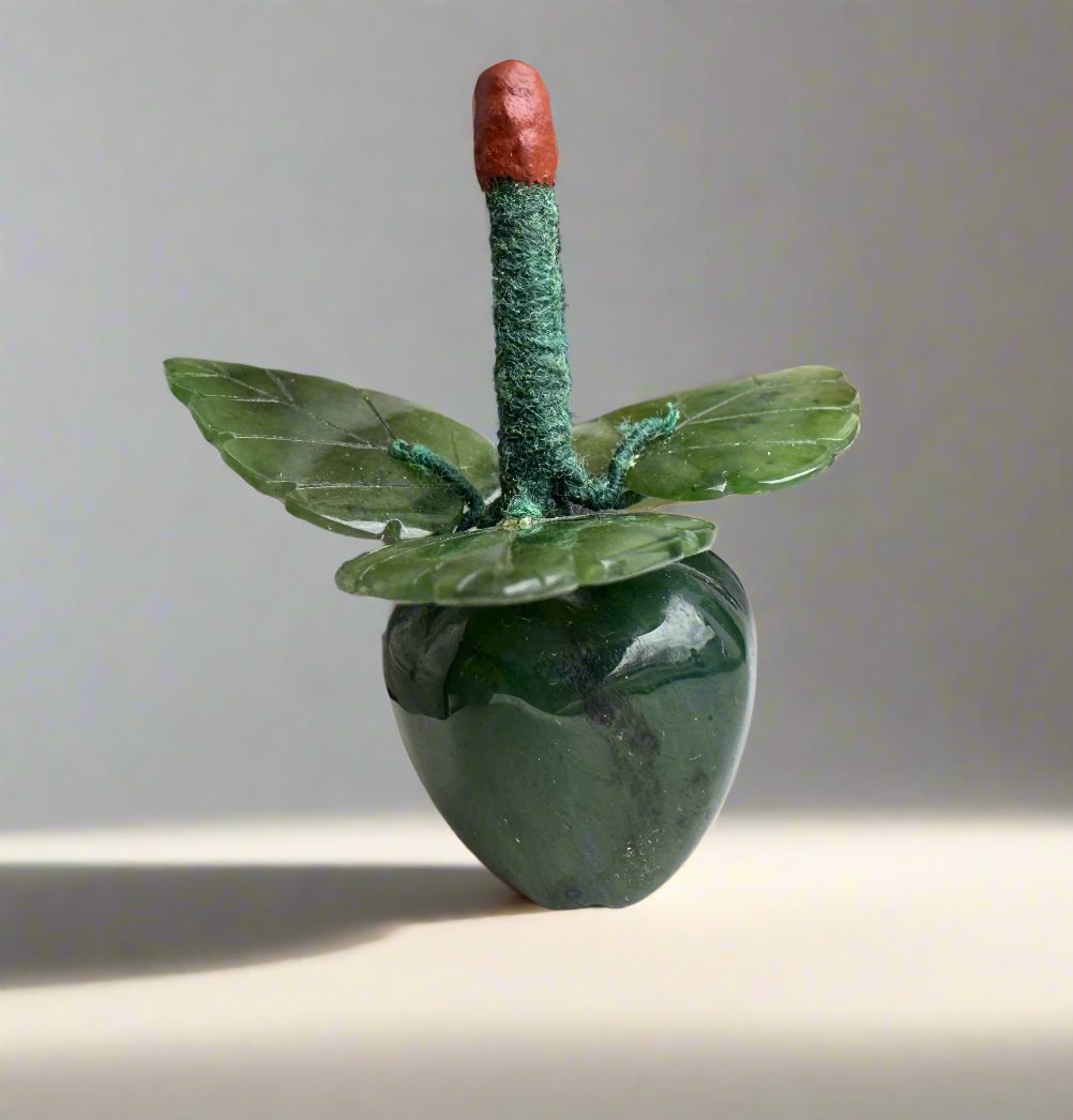 Jade apple carving with a red tipped stem and green leaves against a pale background