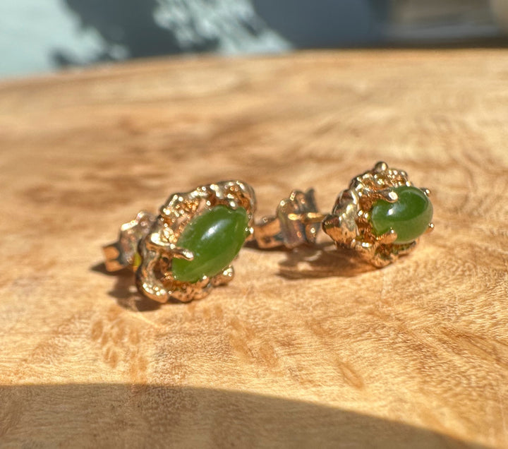 Vintage green jade earrings with ornate gold floral filigree on a wooden surface