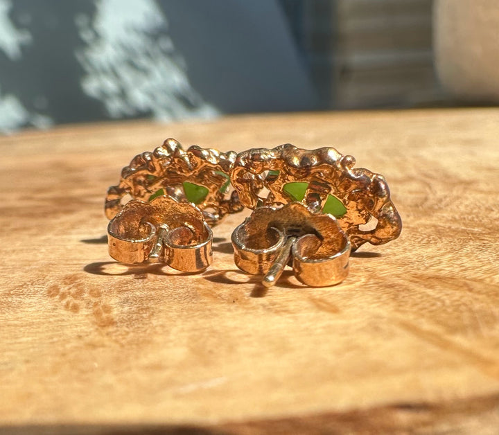 Copper vintage earrings with intricate openwork and jade green stones on a wooden surface.