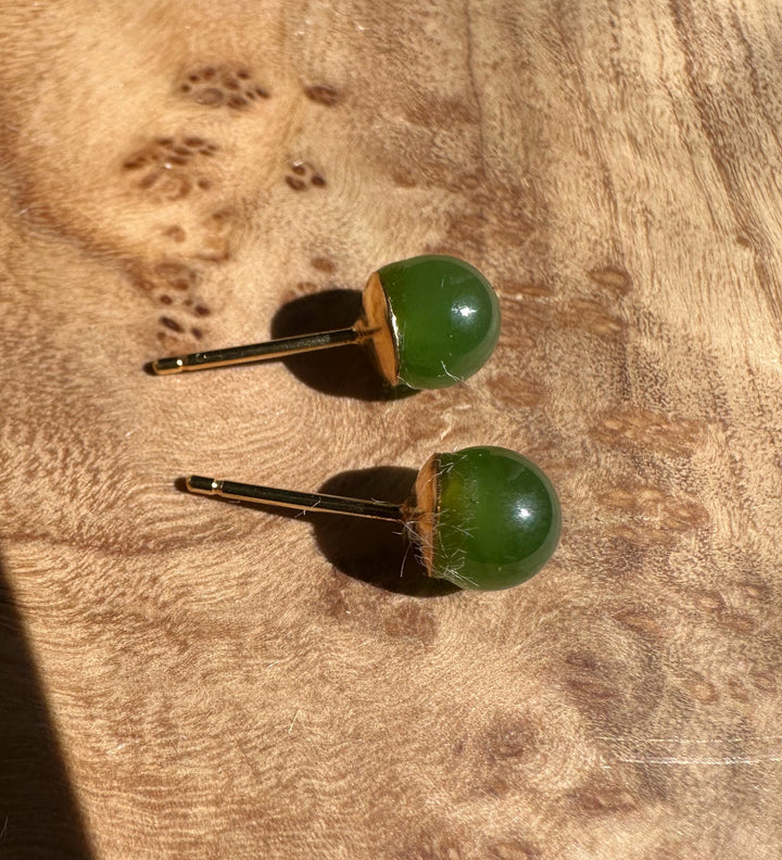 Green jade stud earrings with gold posts on a wooden surface