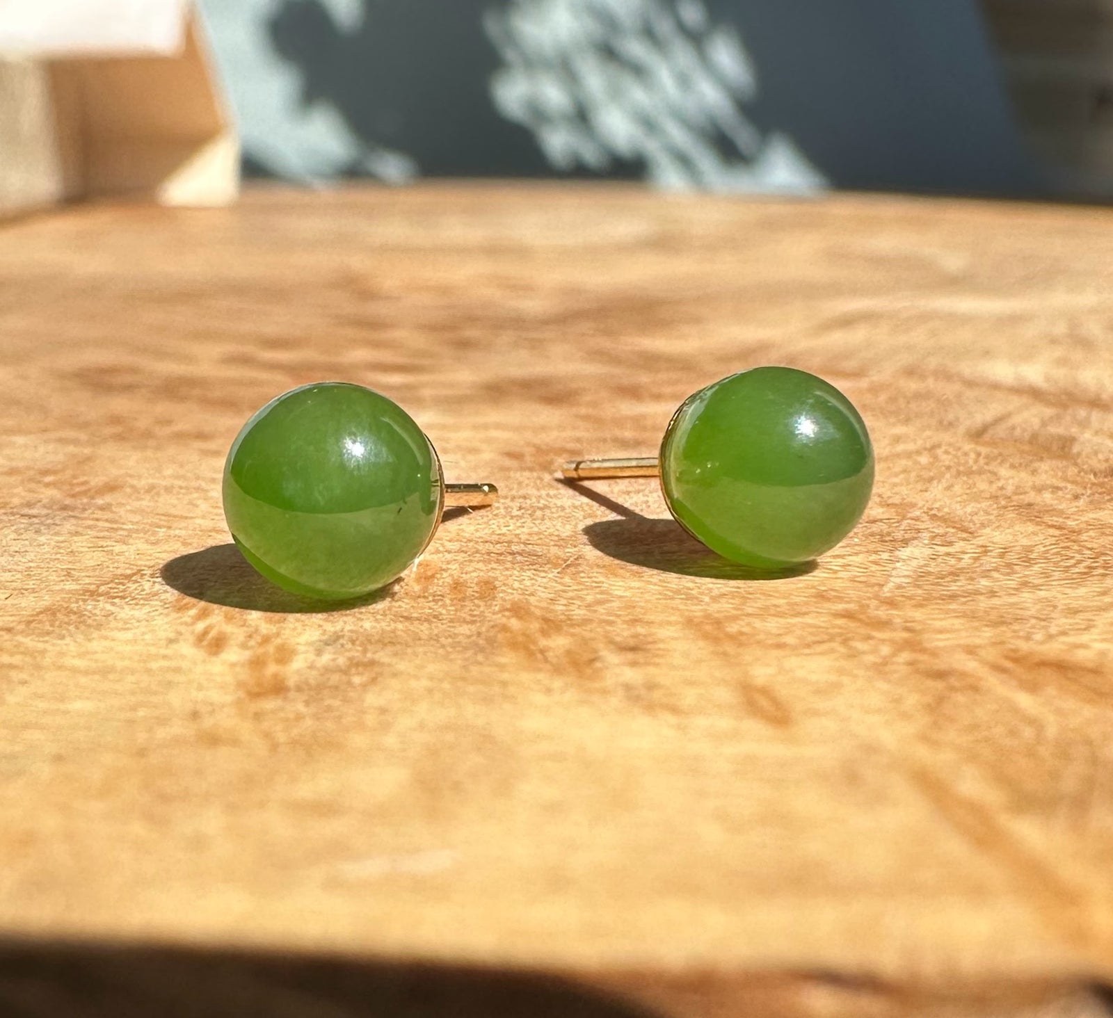 Pair of round green jade stud earrings with gold posts on a wooden surface.