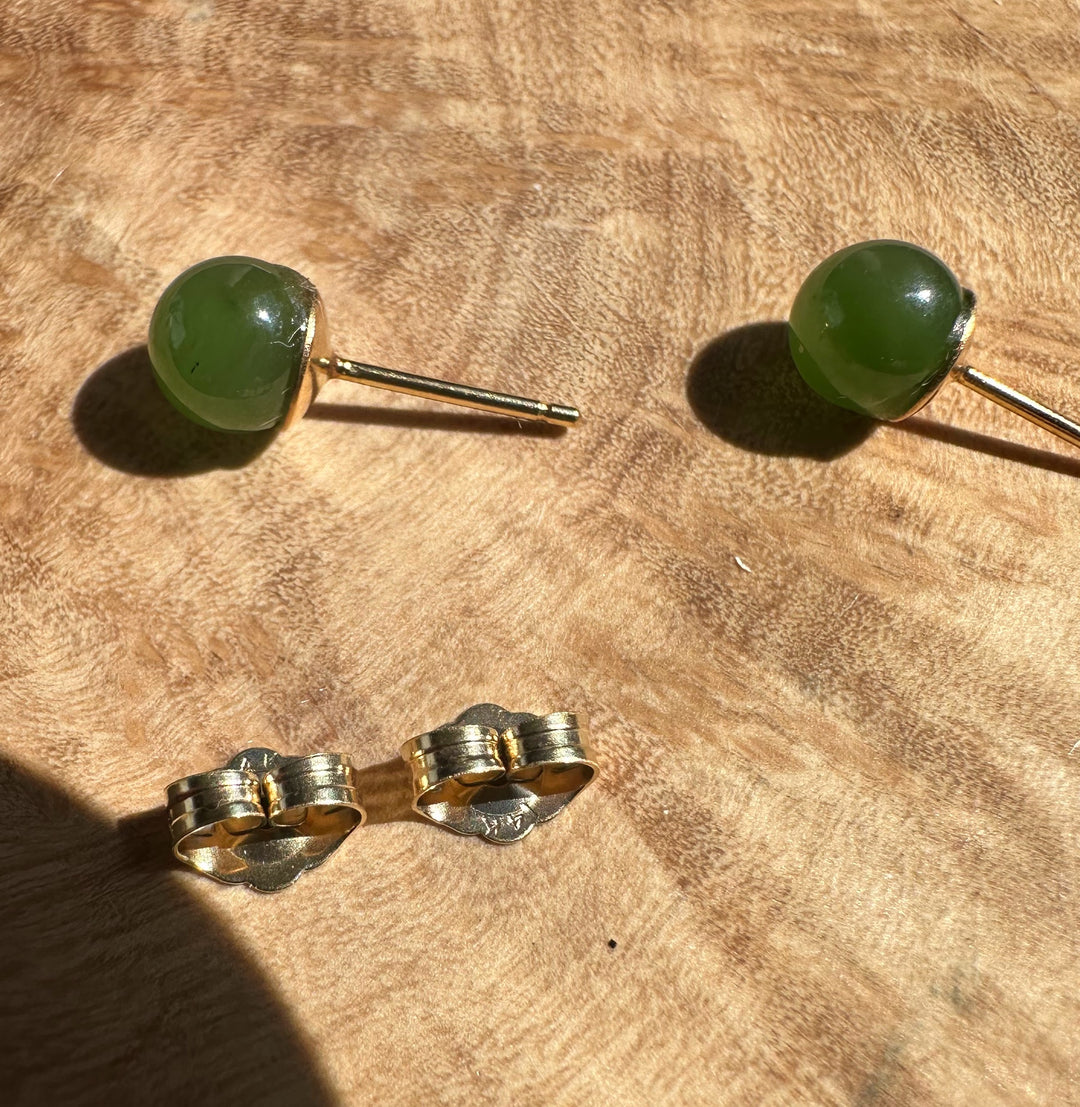 Vintage jade stud earrings with green cabochons and gold posts on a wooden surface