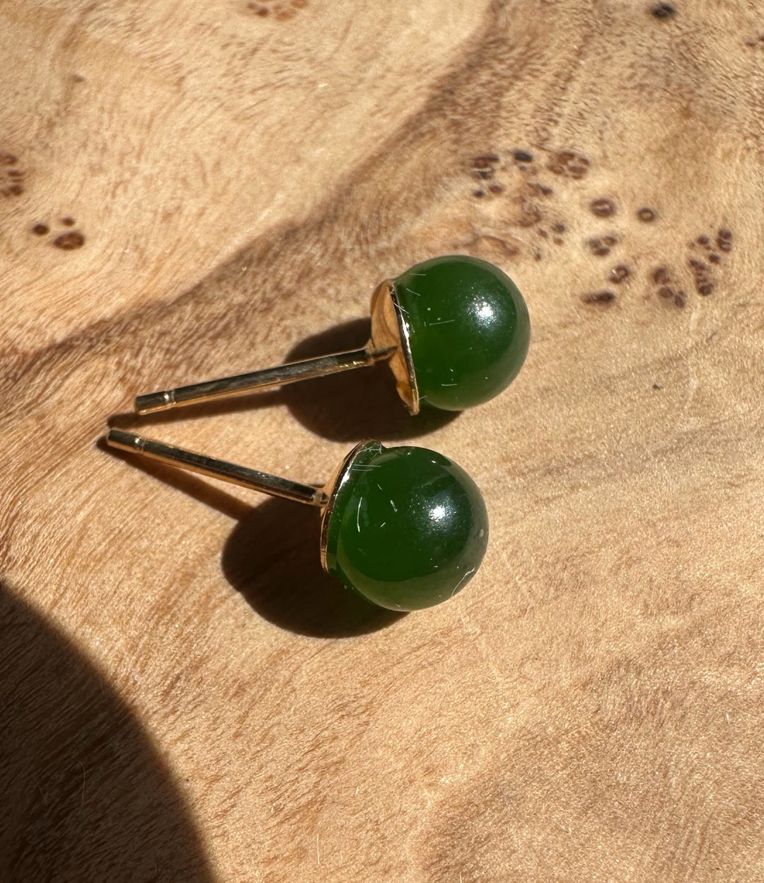 Close up of jade green cabochon stud earrings with gold posts on wood