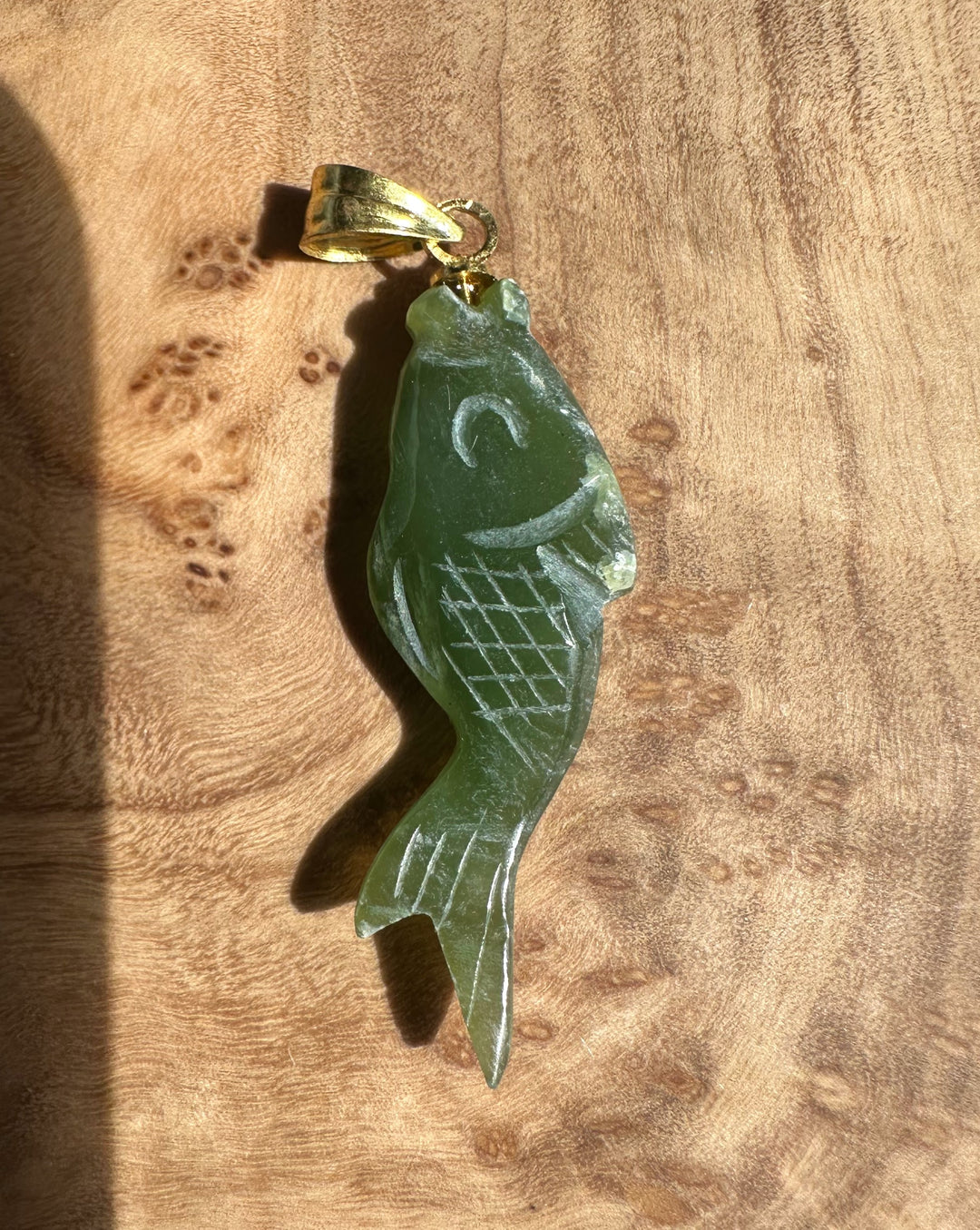 Close-up of a single green fish pendant showing carved scales and a gold bail