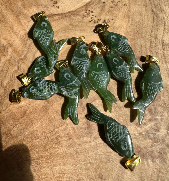 Ten vintage fish pendants carved from dark green stone with gold bail fittings on a wooden surface