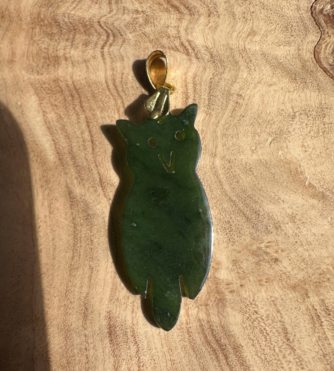 Vintage jade owl pendant with gold bail displayed on a wooden background.
