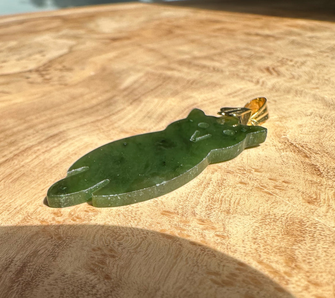 Vintage jade owl pendant with gold bail laid on a wooden surface.