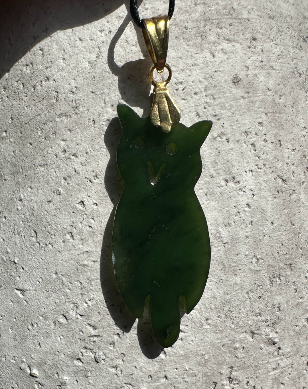 Vintage jade owl pendant with gold bail hanging from a black cord.