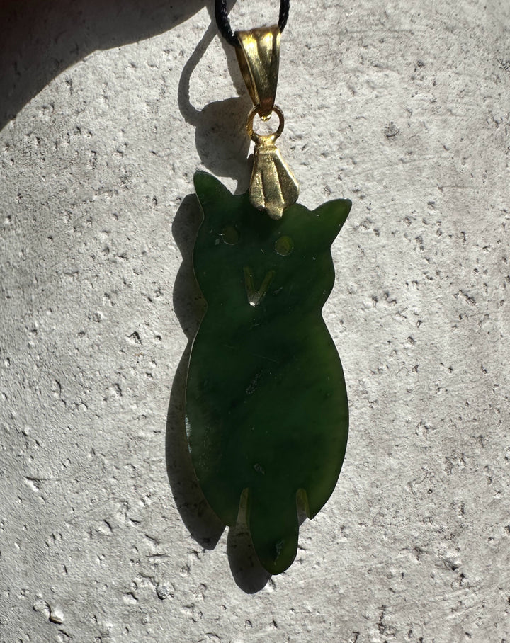 Vintage jade owl pendant with gold bail hanging from a black cord.