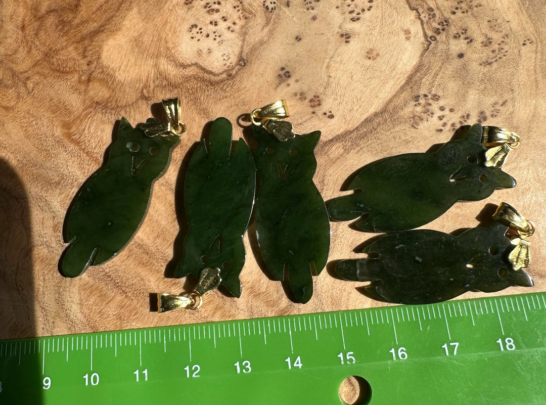 Set of four dark green jade owl pendants with gold bails displayed on wood