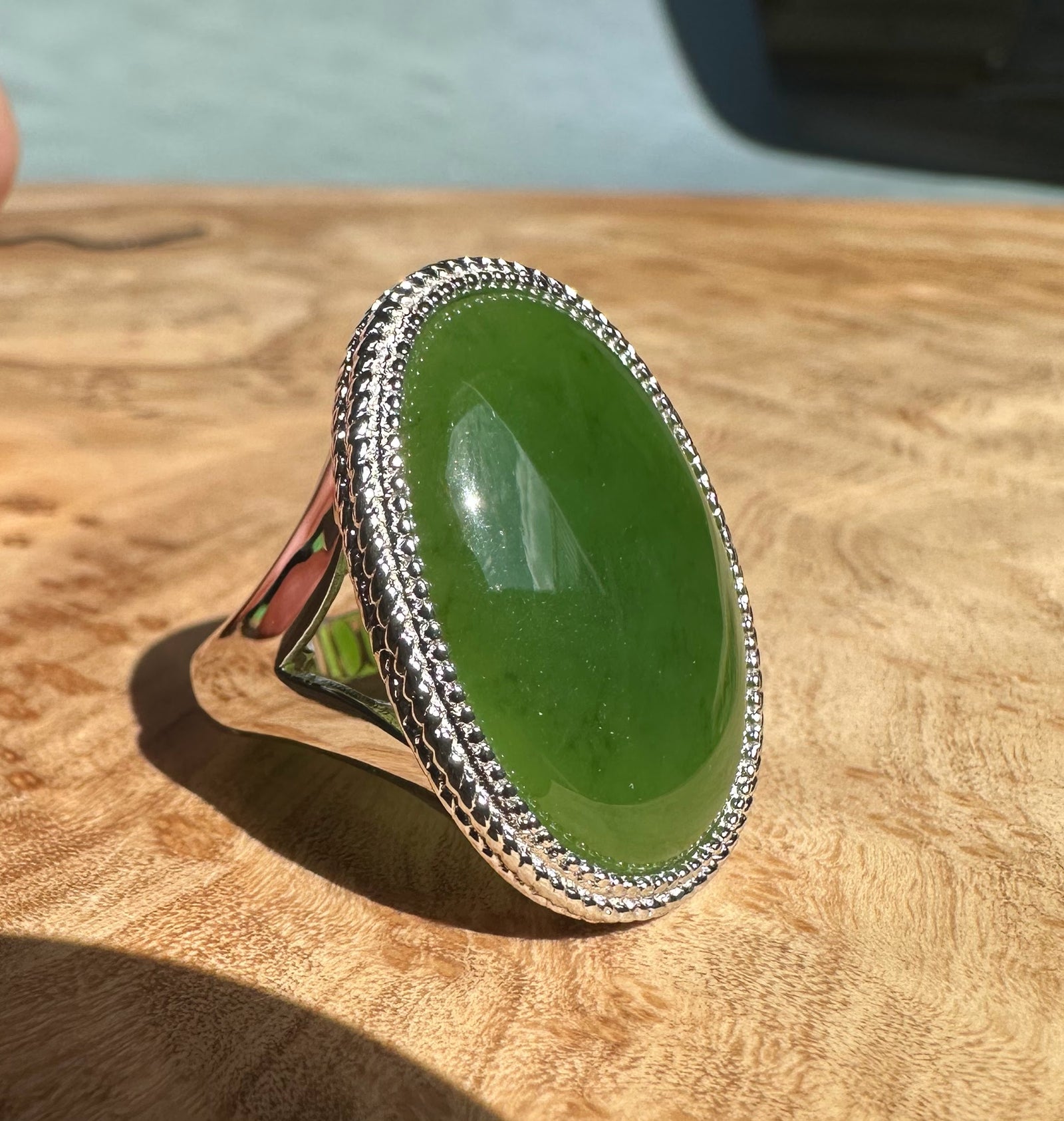 Oval green jade ring with ornate beaded silver bezel set in a bold silver band