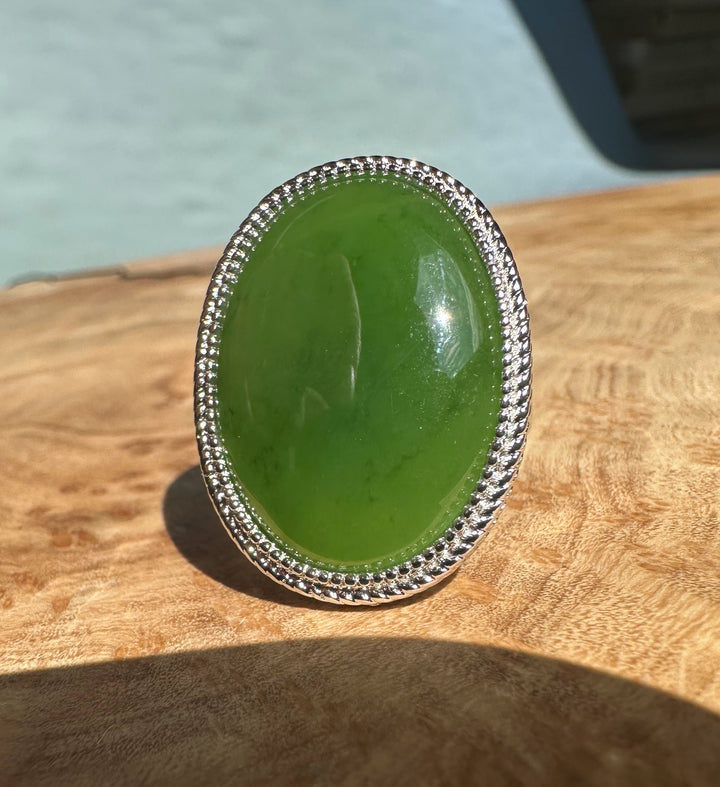 Oval green jade set in a silver beaded bezel on a wooden surface